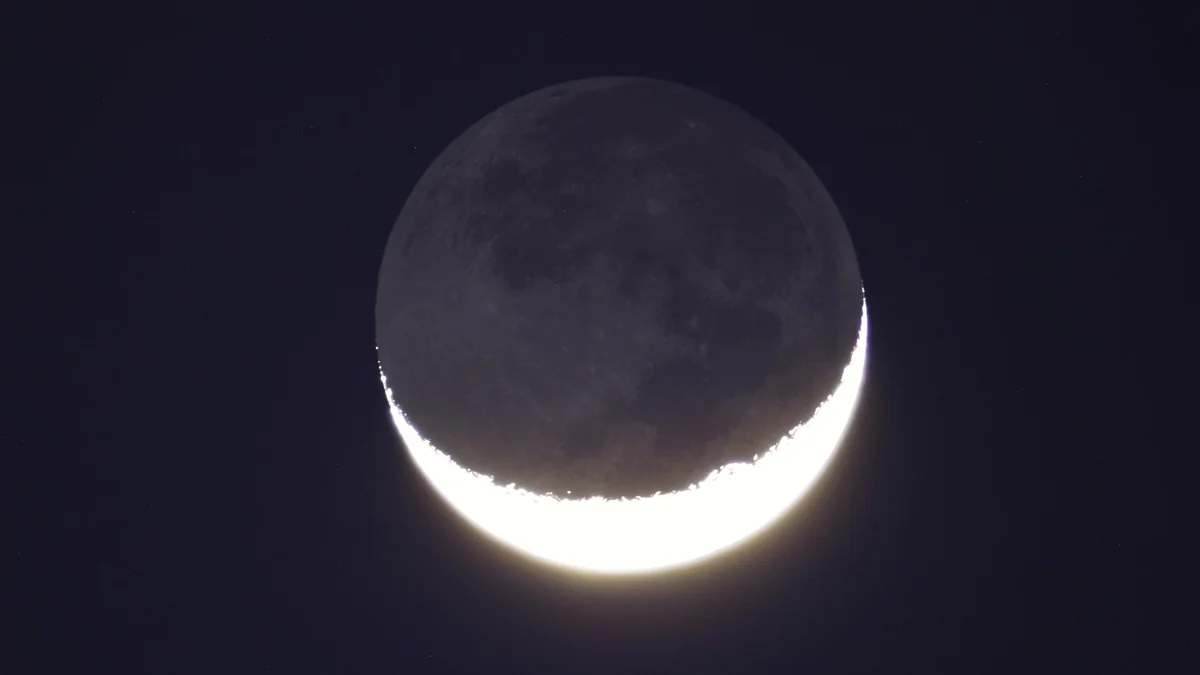 A thin crescent moon against a dark evening sky